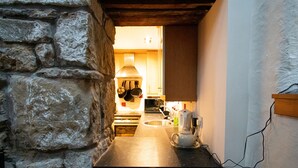 A stone-walled kitchen with a modern stove, a coffee maker, and a view into the adjacent room. - Characterful Semi-Detached House; Enviably Located (St Andrews)