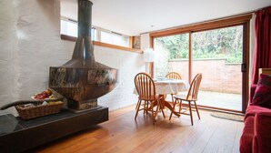 A cozy living room with a fireplace, wooden flooring, a dining table with chairs, and a sliding glass door leading to a garden. - Characterful Semi-Detached House; Enviably Located (St Andrews)