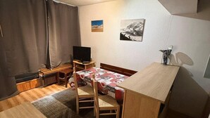 Een kleine kamer met een bed, een bureau, een stoel, een televisie en een radiator.