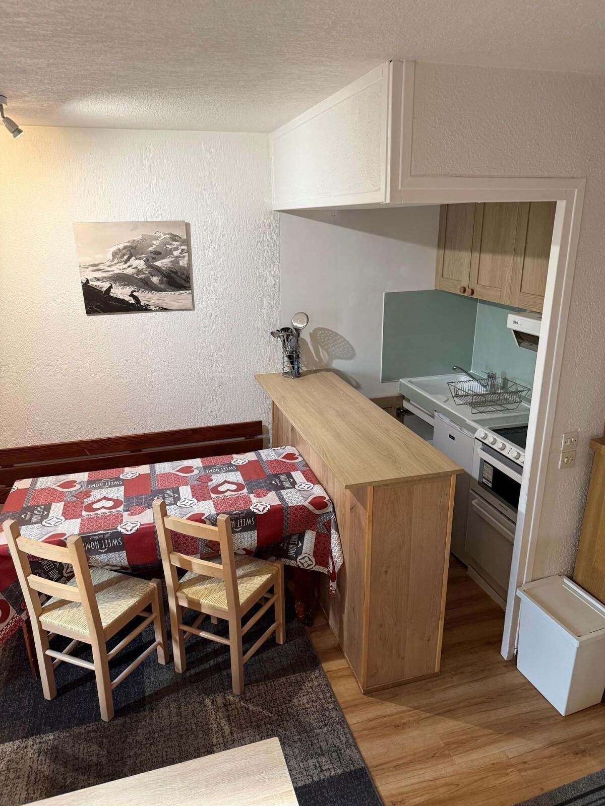 A compact kitchen with wooden cabinets, a small dining table with chairs, and a refrigerator.