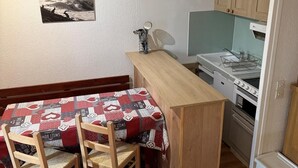 Een compacte keuken met houten kastjes, een kleine eettafel met stoelen en een koelkast.
