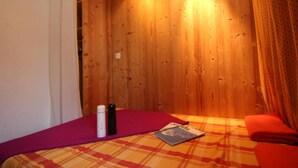 Ein Zimmer mit Holzwänden, einem Bett mit kariertem Überwurf, einem roten Kopfkissen und einer Zeitschrift auf dem Bett.