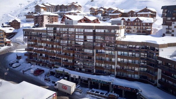 Ein mehrstöckiges Hotel mit Balkonen, im Hintergrund eine Seilbahn und verschneite Umgebung.