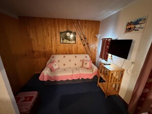 A cozy room with a wooden wall, a sofa with a patterned cover, a small wooden table, and a television.