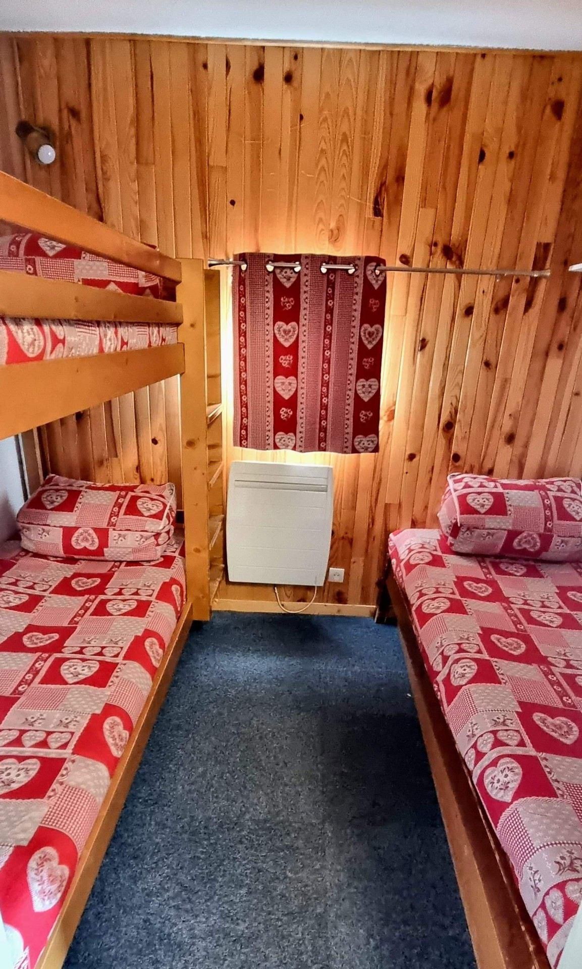 Habitació amb parets de fusta, lliteres, un escriptori petit i una cortina vermella amb dibuixos de cors.
