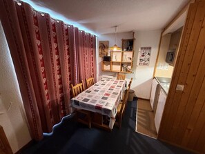 A compact kitchen with a dining area, featuring a table with a patterned tablecloth, wooden chairs, and a small refrigerator.