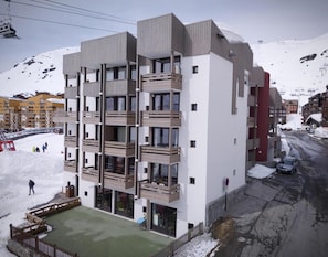 Een meerhoog gebouw met balkons, een skilift op de achtergrond en een besneeuwde berg.