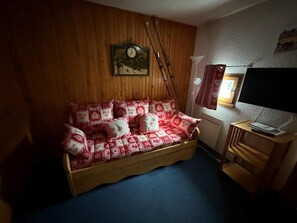 A cozy room with a wooden bed, a wall clock, and a television on a wooden stand.