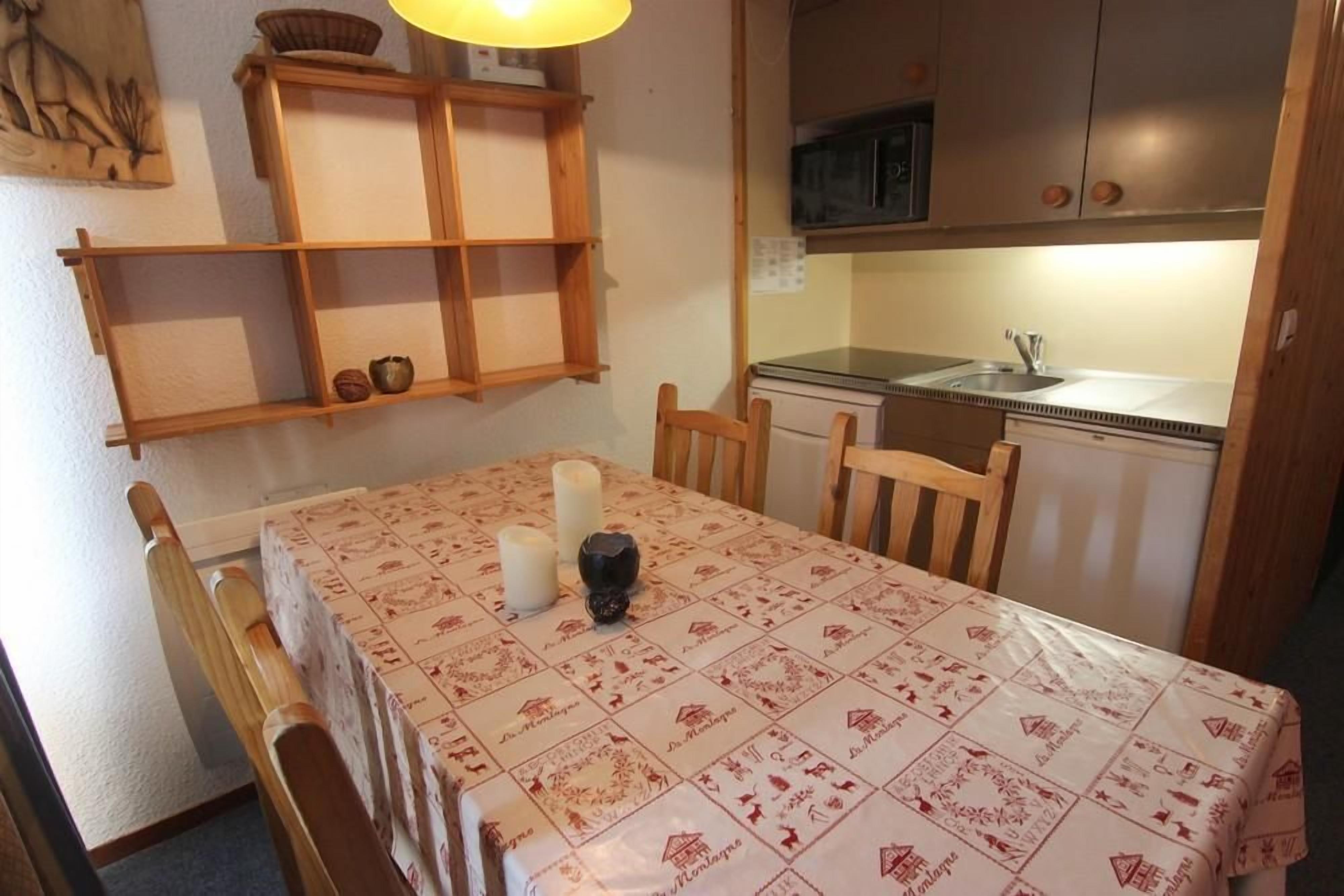 A dining area with a table set for four, wooden chairs, a candle, and a shelf with decorative items.
