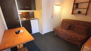Ein gemütlicher, kompakter Wohnraum mit Küchenzeile, einer Couch, einem Holztisch und einer Bank.