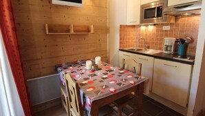 Une cuisine de taille réduite avec des murs en bois, un four à micro-ondes, un évier et une table recouverte d’une nappe à motifs.
