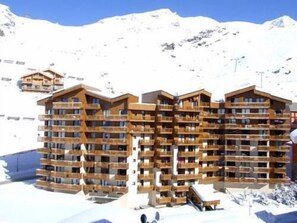 Un hotel de varios pisos con balcones de madera, con una imponente montaña nevada de fondo.