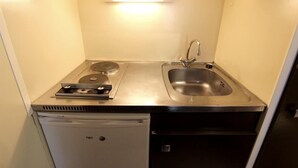 Una kitchenette compacta con estufa, lavabo y refrigerador pequeño.
