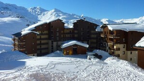 Ein mehrstöckiges Hotel mit einem zentralen Eingang und Balkonen, umgeben von schneebedeckten Bergen.