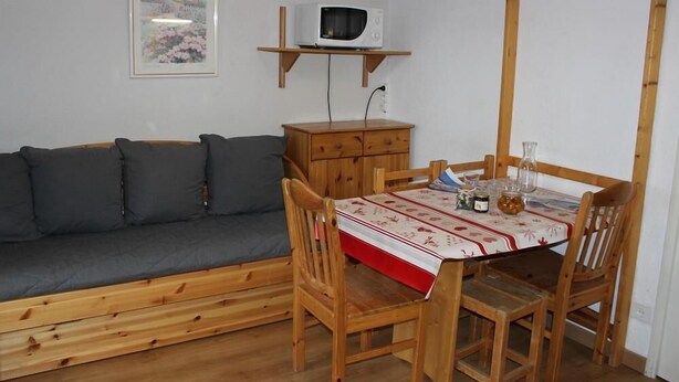 Ein Holzespeisesaal mit Stühlen, eine Holzkommode, ein graues Sofa und eine Mikrowelle auf einem Regal.