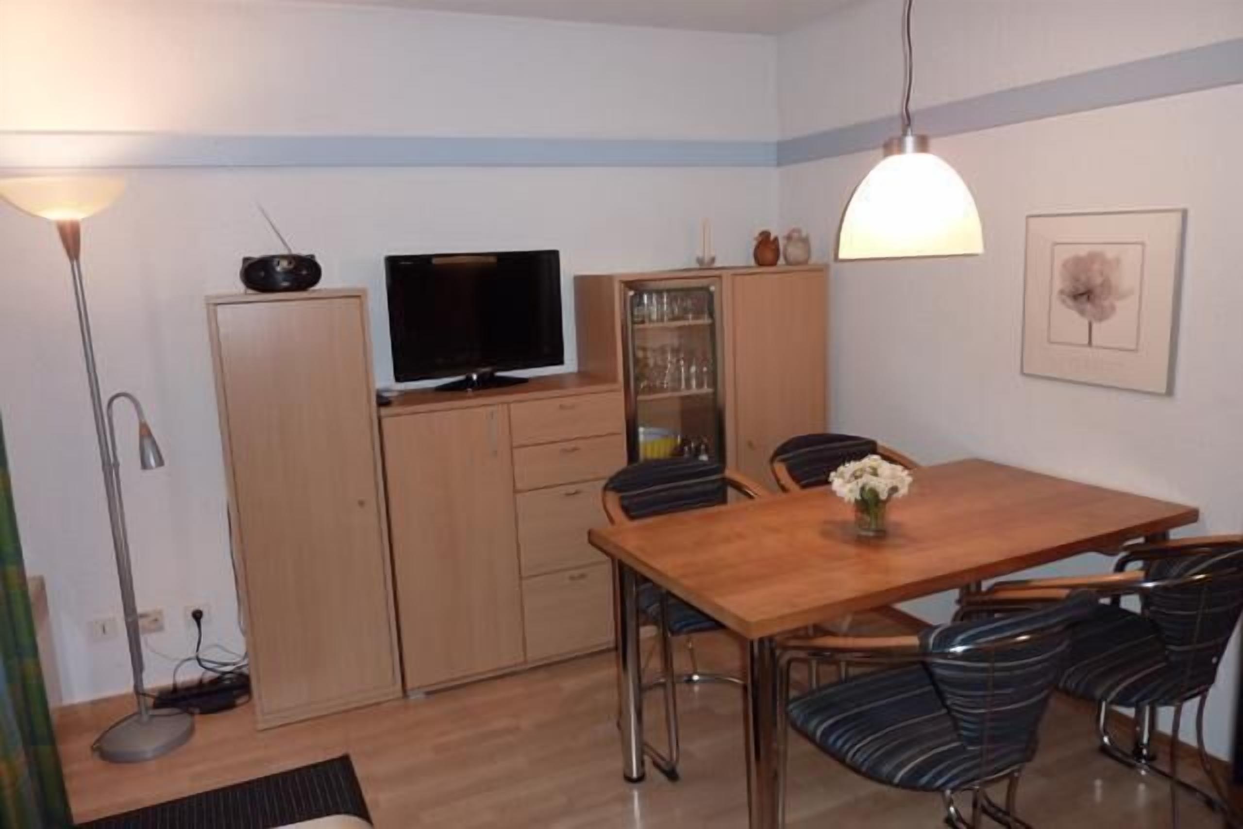 Une cuisine de taille réduite avec une table en bois, des chaises, un téléviseur et des placards.