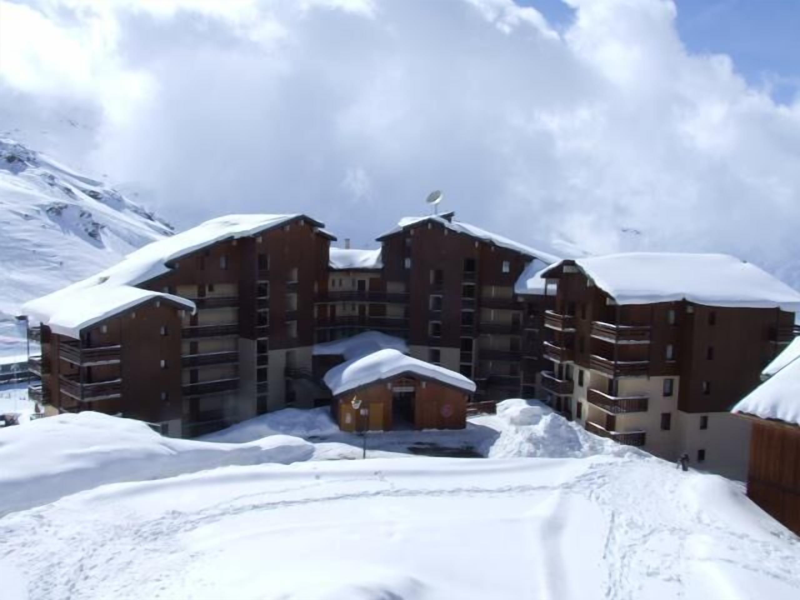 A multi-story hotel with a snow-covered roof, surrounded by snow and mountains.