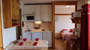 A compact kitchen with white cabinets, a microwave, and a sink. There is a dining table with red bowls and a patterned tablecloth.