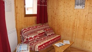 A cozy room with a wooden bed, a small wooden table, and a window with red curtains.