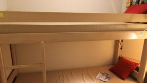 A bunk bed with a ladder, a single red pillow, and a magazine on the lower bunk.