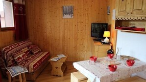 A cozy room with a wooden floor, a sofa with patterned cushions, a small wooden table, a television, and a table with red bowls.
