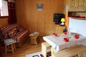 Una habitación acogedora con piso de madera, un sofá con cojines estampados, una mesita de madera, un televisor y una mesa con cuencos rojos.