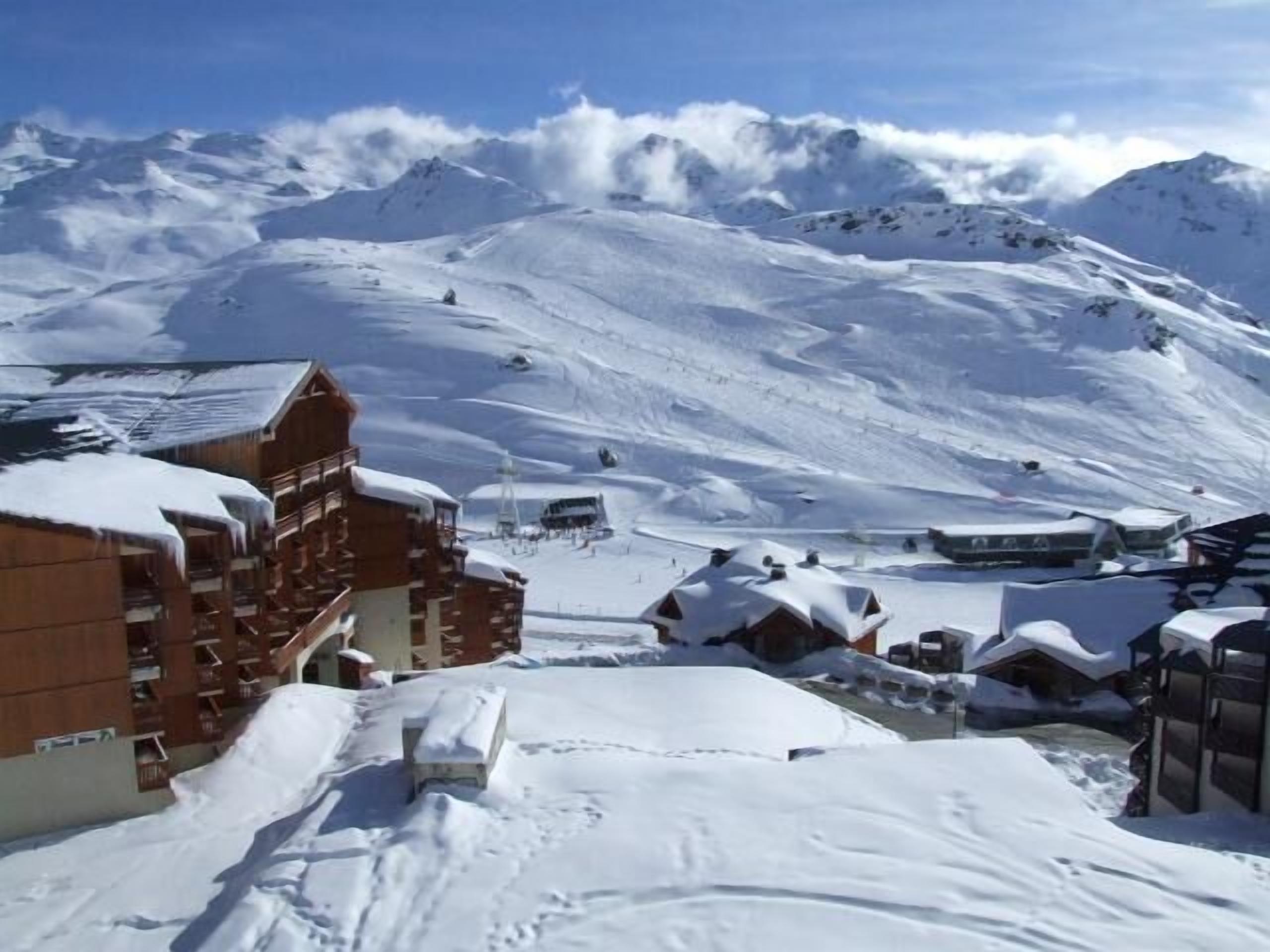 Et sneklædt feriested med bjergudsigt, træhuse, ski bakker og en klar himmel.