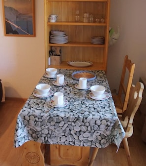 Une table à manger dressée avec des bols et des tasses blancs, une nappe à motifs et, en arrière-plan, une bibliothèque en bois.