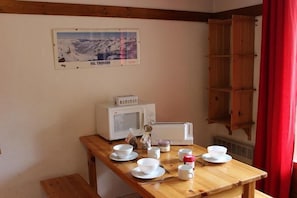 A wooden table with white cups and saucers, a microwave, and a small cabinet.