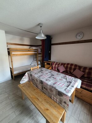 A cozy room with a bunk bed, a sofa, a table with a patterned tablecloth, and a hanging lamp.