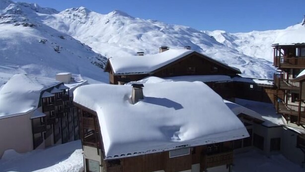 Et snedækket fjeldhotel med flere træbygninger, en skilift og en klar blå himmel.