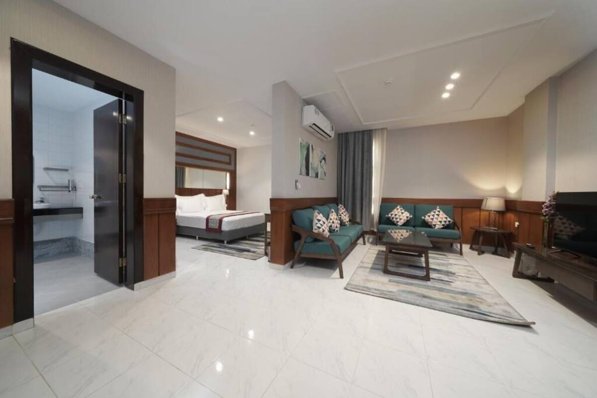 A modern hotel room with a bed, a sofa, a coffee table, and a TV.