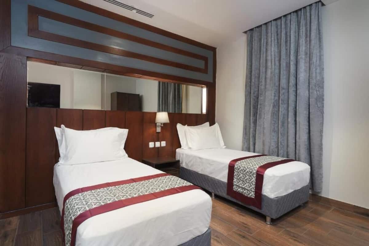 A hotel room with two beds, a large mirror, and a window with curtains.