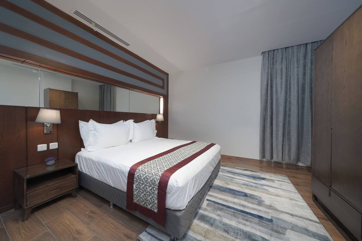 A hotel room with a large bed, a wooden headboard, a nightstand, a mirror, and a wardrobe.