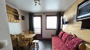 Una habitación con una mesa de comedor y sillas de madera, un sofá rojo y un televisor instalado en la pared.