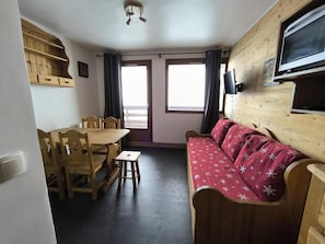Ett rum med ett matbord och stolar i trä, en röd soffa och en tv som är monterad på väggen.