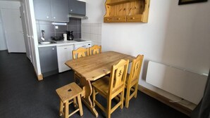 Una cocina compacta con armarios grises, una mesa de comedor de madera con cuatro sillas, un taburete pequeño y un estante de madera sobre la mesa.