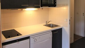 Cozinha compacta com armários escuros, micro-ondas, pia e máquina de lavar louça.