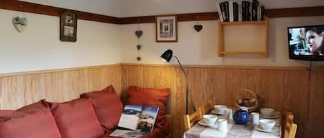 A cozy room with a wooden bench, a table set for dining, a television, and a lamp.