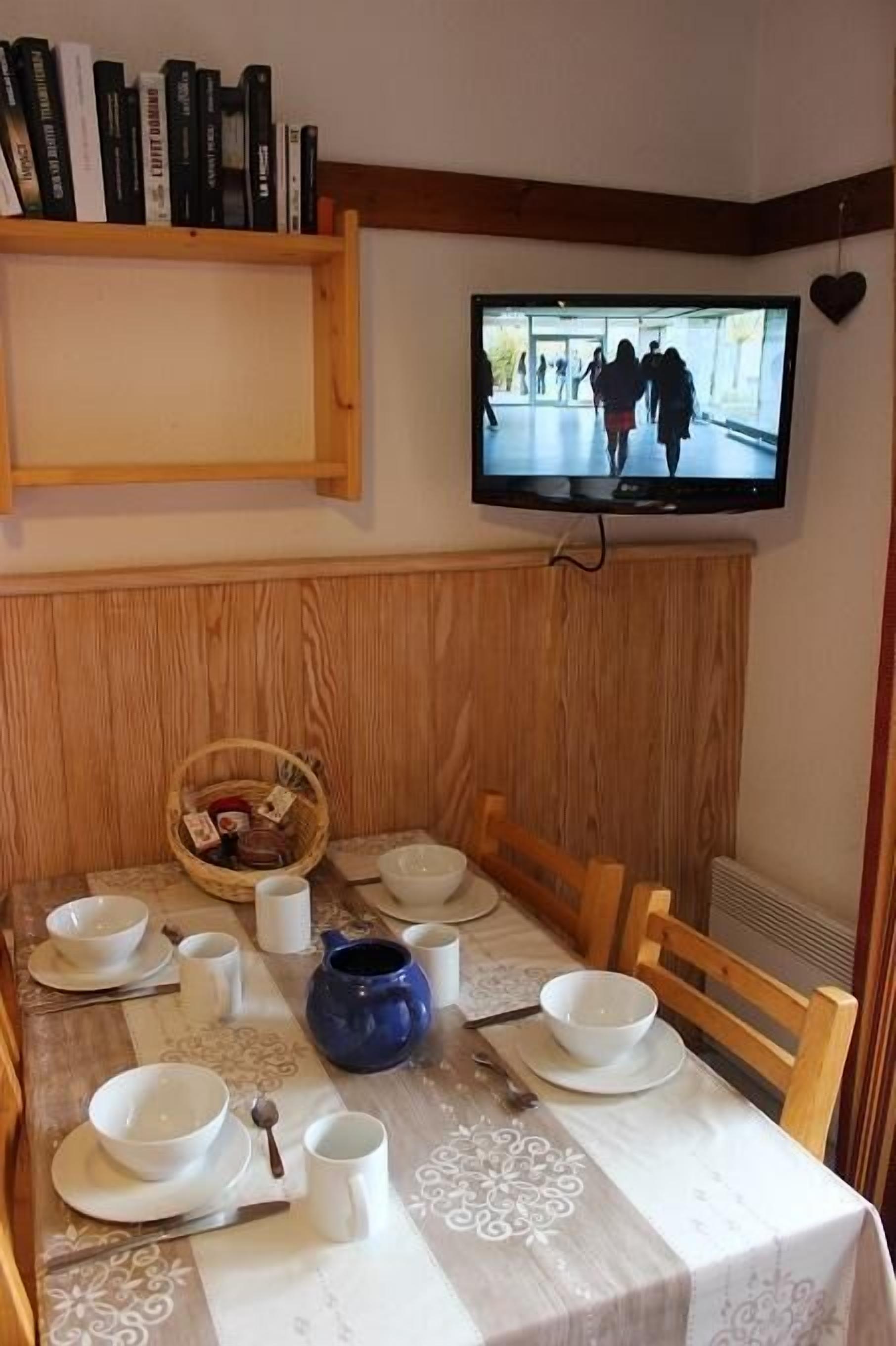 En matplats med ett bord för fyra personer, en tv som  är monterad på väggen och en bokhylla ovanför bordet.