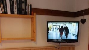 Uma área de refeições com uma mesa posta para quatro pessoas, uma televisão na parede e uma estante acima da mesa.