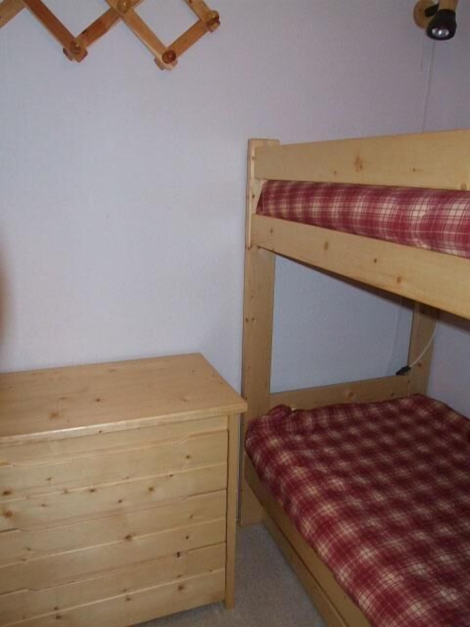 Een stapelbed met een ruitdessin sprei, een houten dressoir en een wandplank.