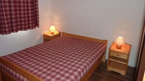 A small, single-bed room with a checkered bedspread, two bedside tables with lamps, and a plaid curtain. - 150m from ski slopes, 3rd floor, view ski slopes, balcony, 29m², Val Thorens (Val Thorens)