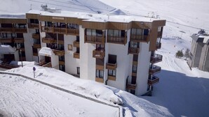 A multi-story hotel with balconies, set against a snowy mountain backdrop.