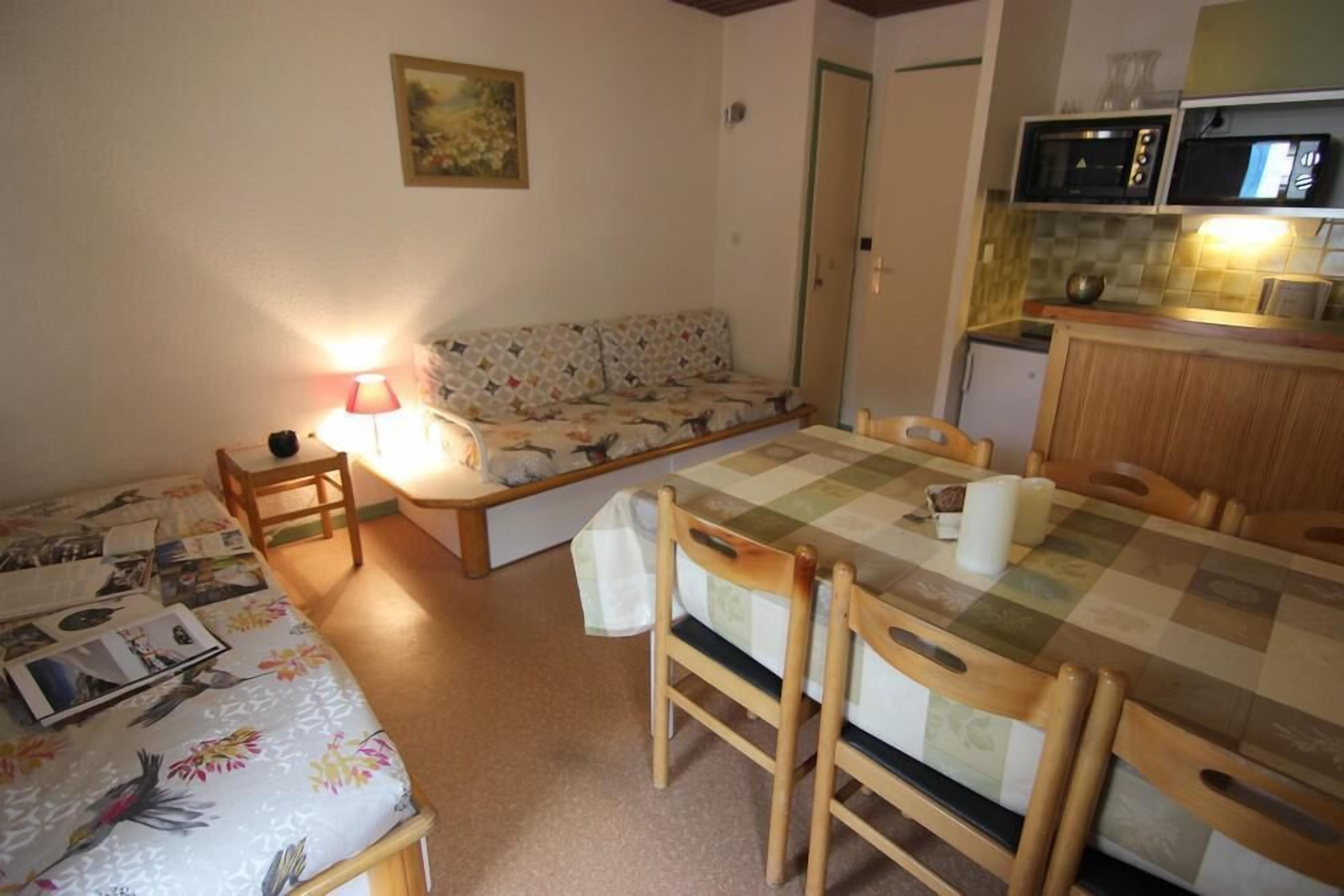 Een gezellige kamer met een bed, een bank, een eettafel met stoelen, een lamp en een kitchenette met een magnetron.