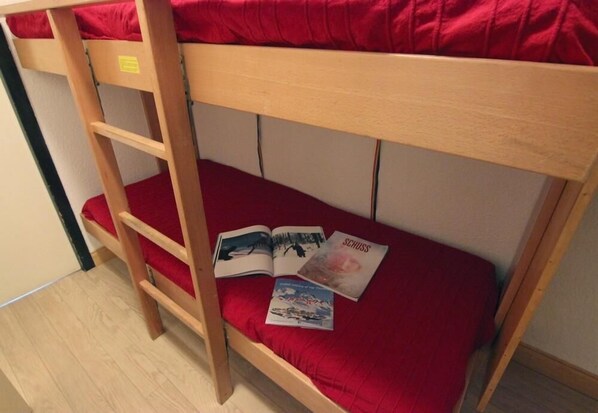 Un letto a castello con materasso rosso, una scala in legno e un piccolo ripiano.