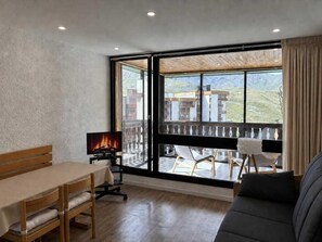 Una habitación con una mesa de comedor, sillas, un sofá, un televisor y un balcón con vistas a edificios y un incendio.