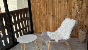 Una habitación con paneles de madera, un sillón blanco y mullido, un banco gris acolchado y una pequeña mesa redonda.