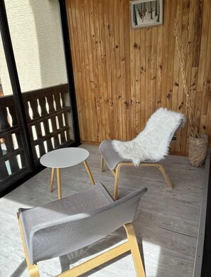 A wooden-paneled room with a white furry chair, a grey cushioned bench, and a small round table.