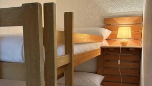 Una cama litera con escalera de madera, una mesita de noche con lámpara y un estante fijado a la pared.